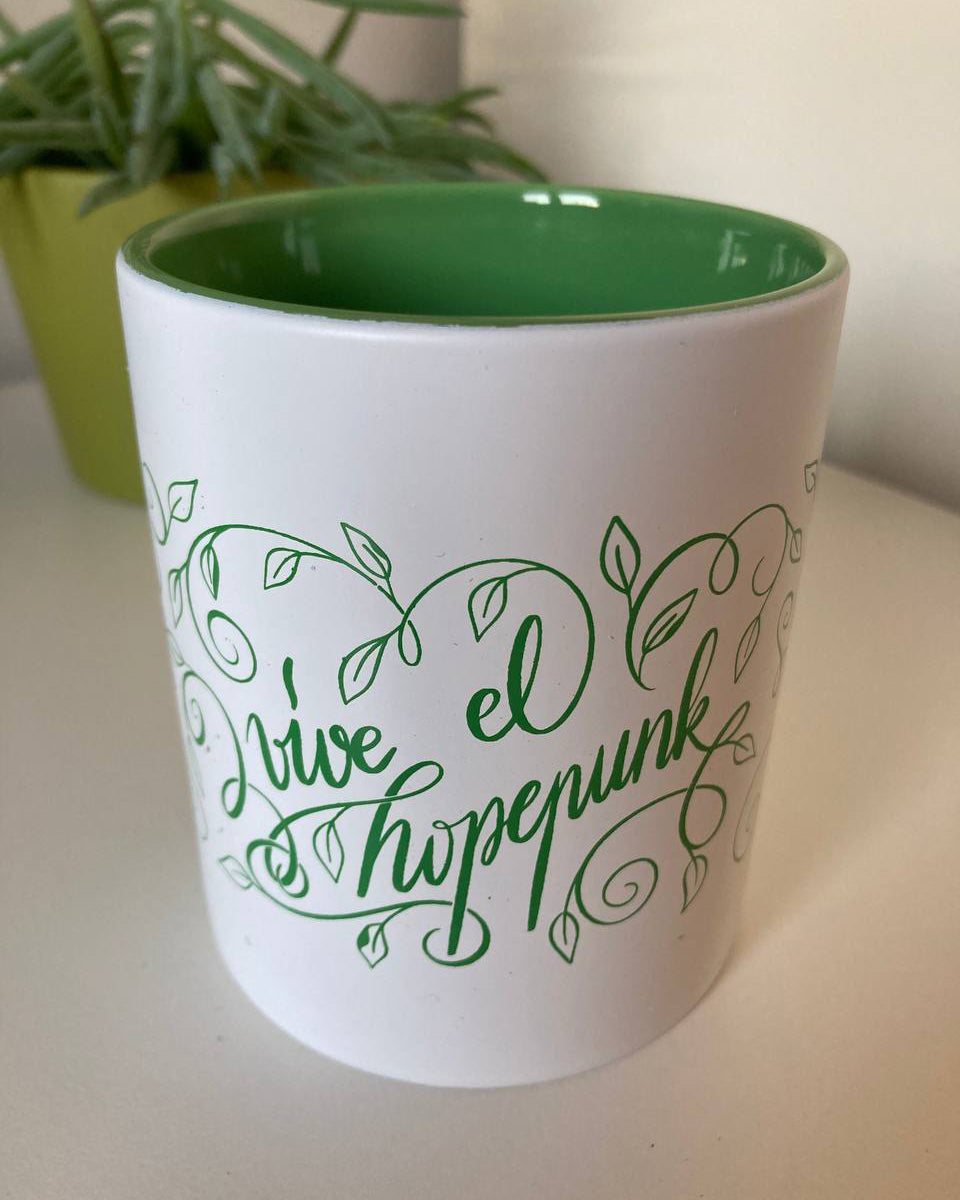 Taza con el interior verde y el exterior blanco, con el mensaje "vive el hopepunk" caligrafiado y rodeado de brotes y hojitas verdes.