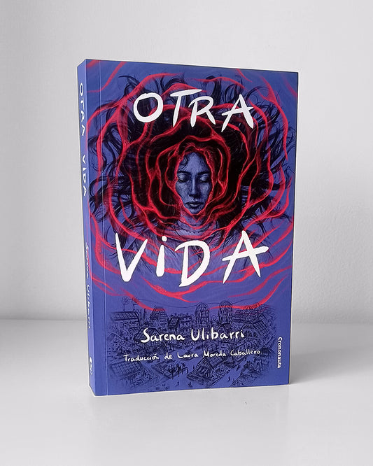 La imagen principal es el rostro de una mujer joven con los ojos cerrados enmarcado por una superficie de agua. La mujer está semisumergida en ella y el cabello negro y liso flota en suaves ondas a su alrededor. Lleva una camisa y varios colgantes al cuello. El fondo es morado y contrasta con las líneas naranjas que forman la superficie rizada del agua. Las ondas se van expandiendo conforme se alejan del rostro de la mujer hasta que, en la parte inferior de la imagen, aparece un pequeño pueblo con casas.